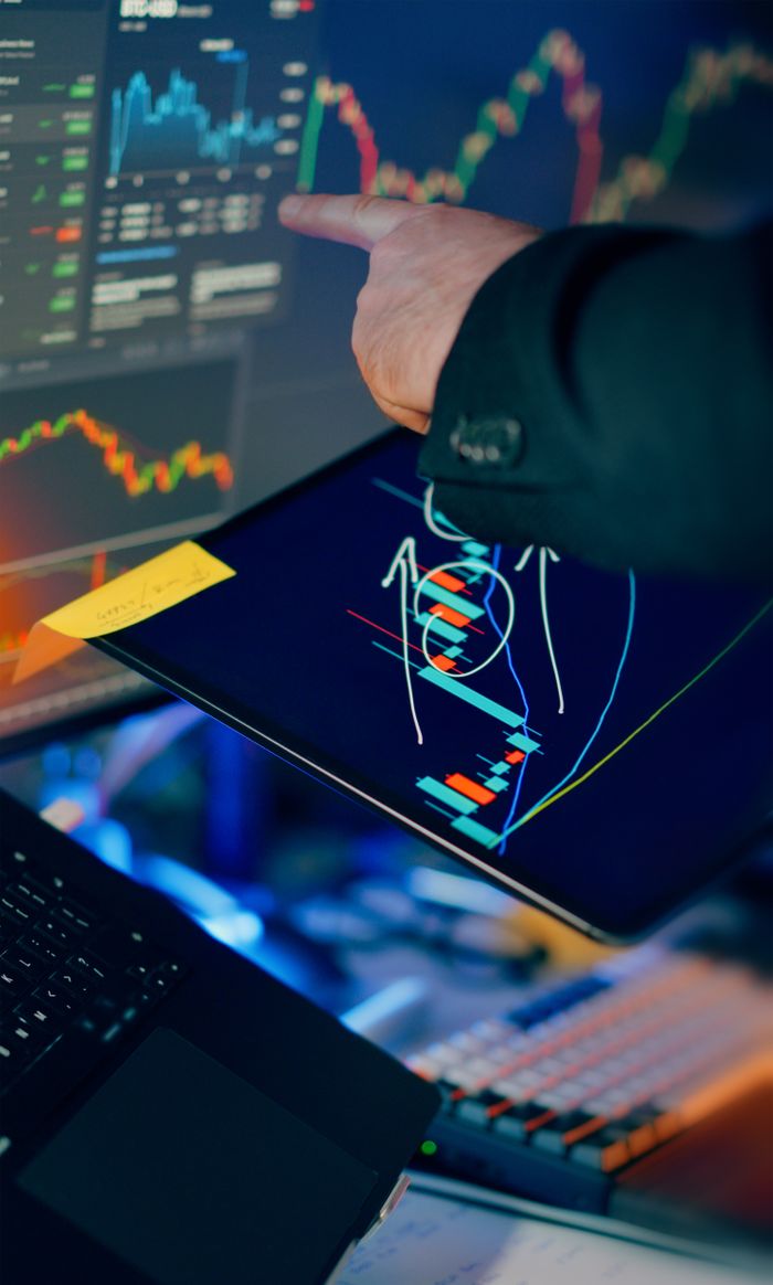 gallery-4 A business professional examines financial charts on a tablet and monitor for investment strategy.
