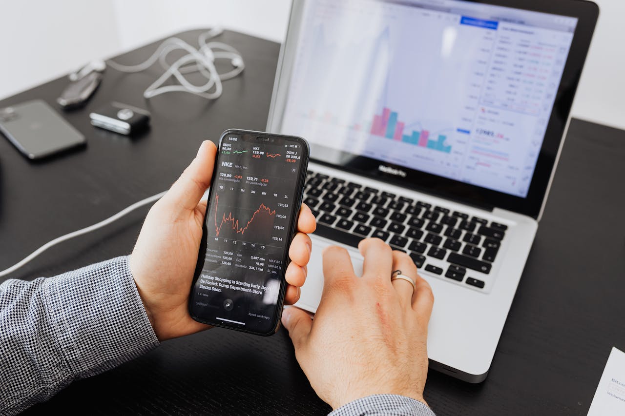 about-02 Person analyzes stock data with a smartphone and laptop, indoors.