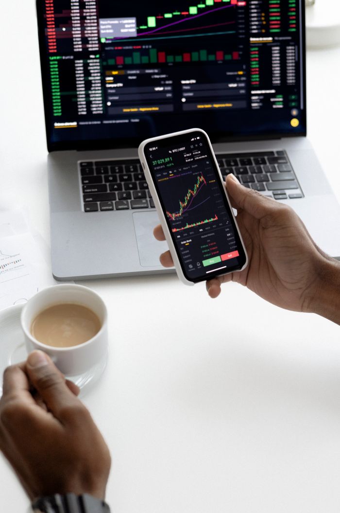 services-02 Person analyzing stock market trends on smartphone with laptop background